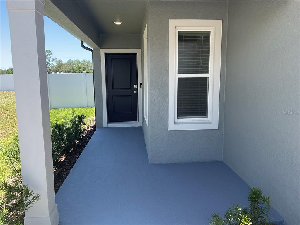 A covered front porch features a dark door, a window, and a painted concrete floor — 3517 HORNBEAM ROAD, SPRING HILL, FL