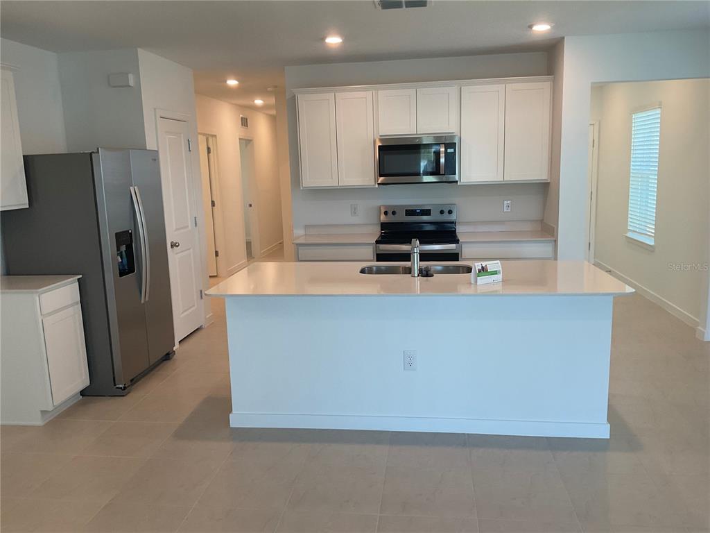 A kitchen features white cabinets, stainless steel appliances, a center island, and light-colored tile flooring — 3517 HORNBEAM ROAD, SPRING HILL, FL