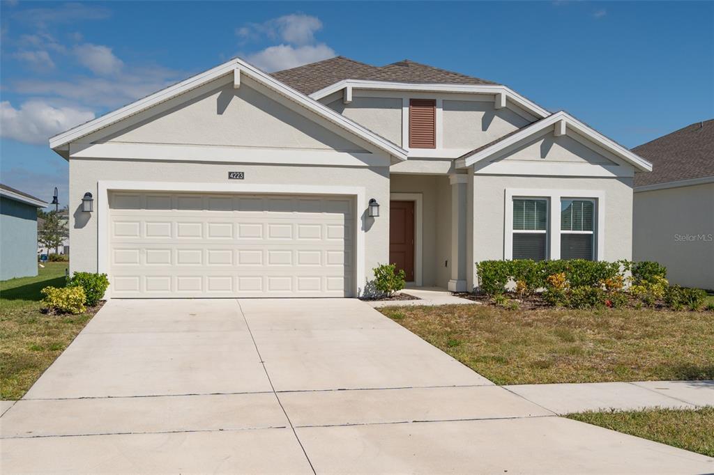 A single-story house with a beige stucco exterior, a two-car garage, and a brown roof — 4223 LITTLE OWL LANE, KISSIMMEE, FL
