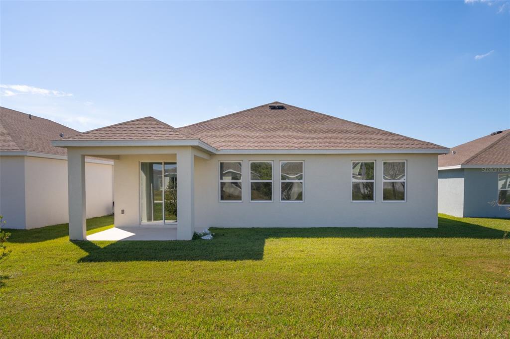 The exterior rear view of a single-story house features a covered patio and lawn — 4223 LITTLE OWL LANE, KISSIMMEE, FL
