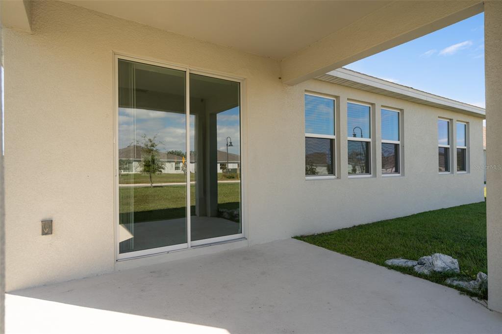 A covered concrete patio features a sliding glass door and several windows on a stucco wall — 4223 LITTLE OWL LANE, KISSIMMEE, FL