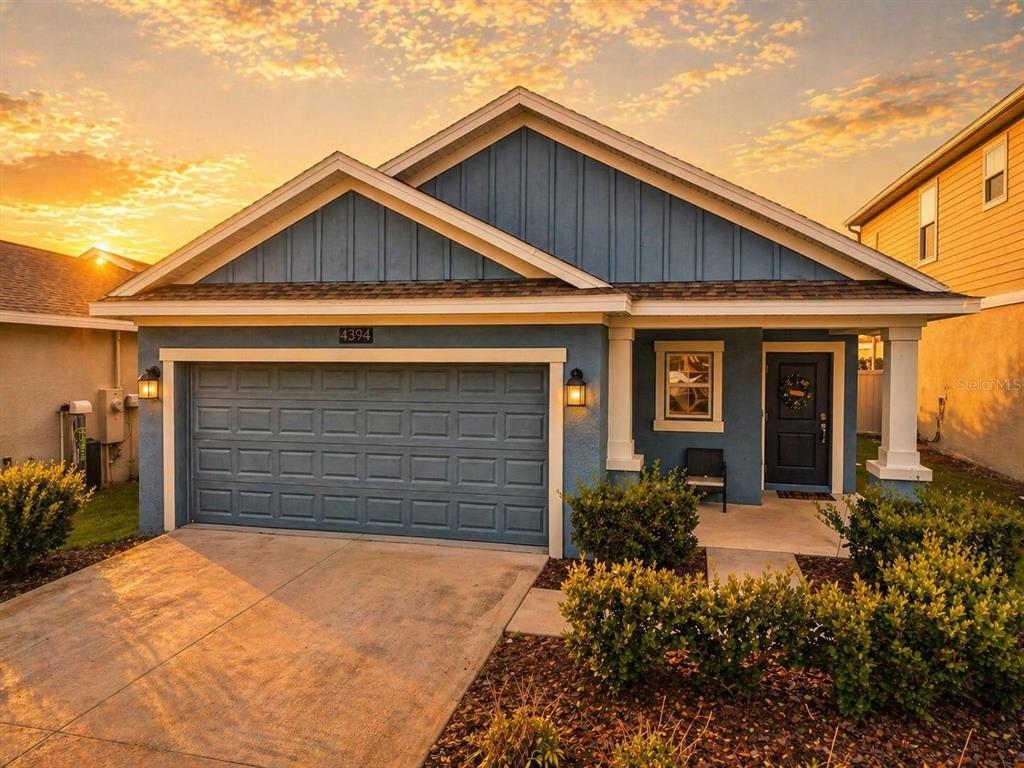 A blue single-story house with a two-car garage and a covered front porch at sunset — 4394 BABBLING BROOK WAY, KISSIMMEE, FL