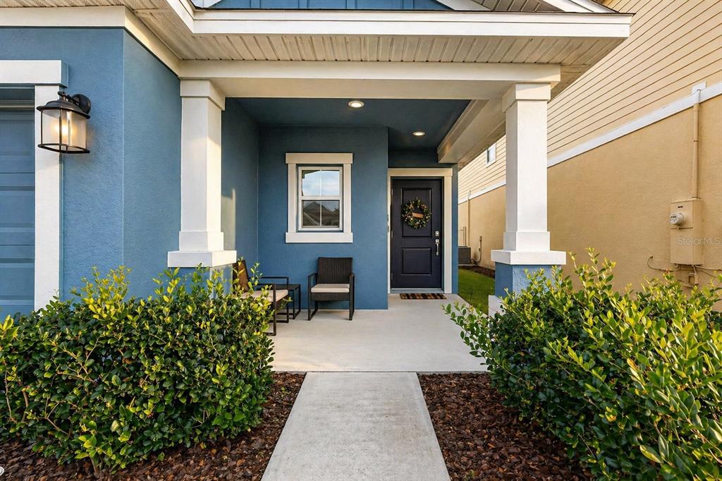 A blue house exterior features a covered front porch with two chairs and a door — 4394 BABBLING BROOK WAY, KISSIMMEE, FL