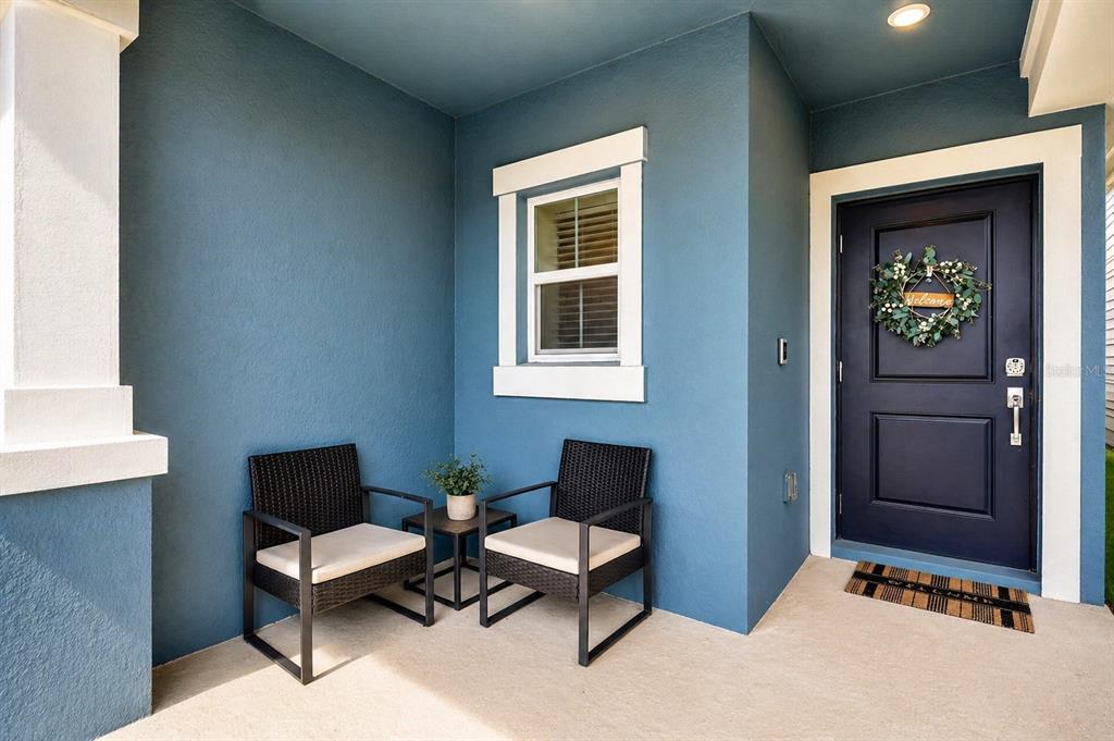 A blue-walled front porch features two wicker chairs, a small side table, and a dark door — 4394 BABBLING BROOK WAY, KISSIMMEE, FL