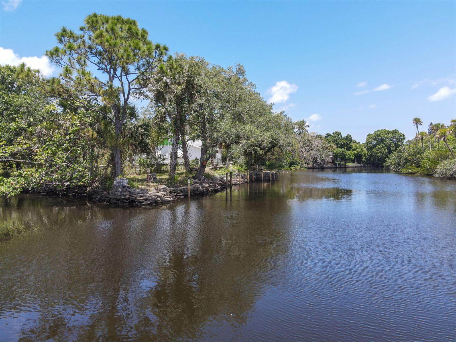 A calm river flows past a tree-lined bank with a stone retaining wall and house — 332 SW Salerno Road, Stuart FL 34997, STUART, FL