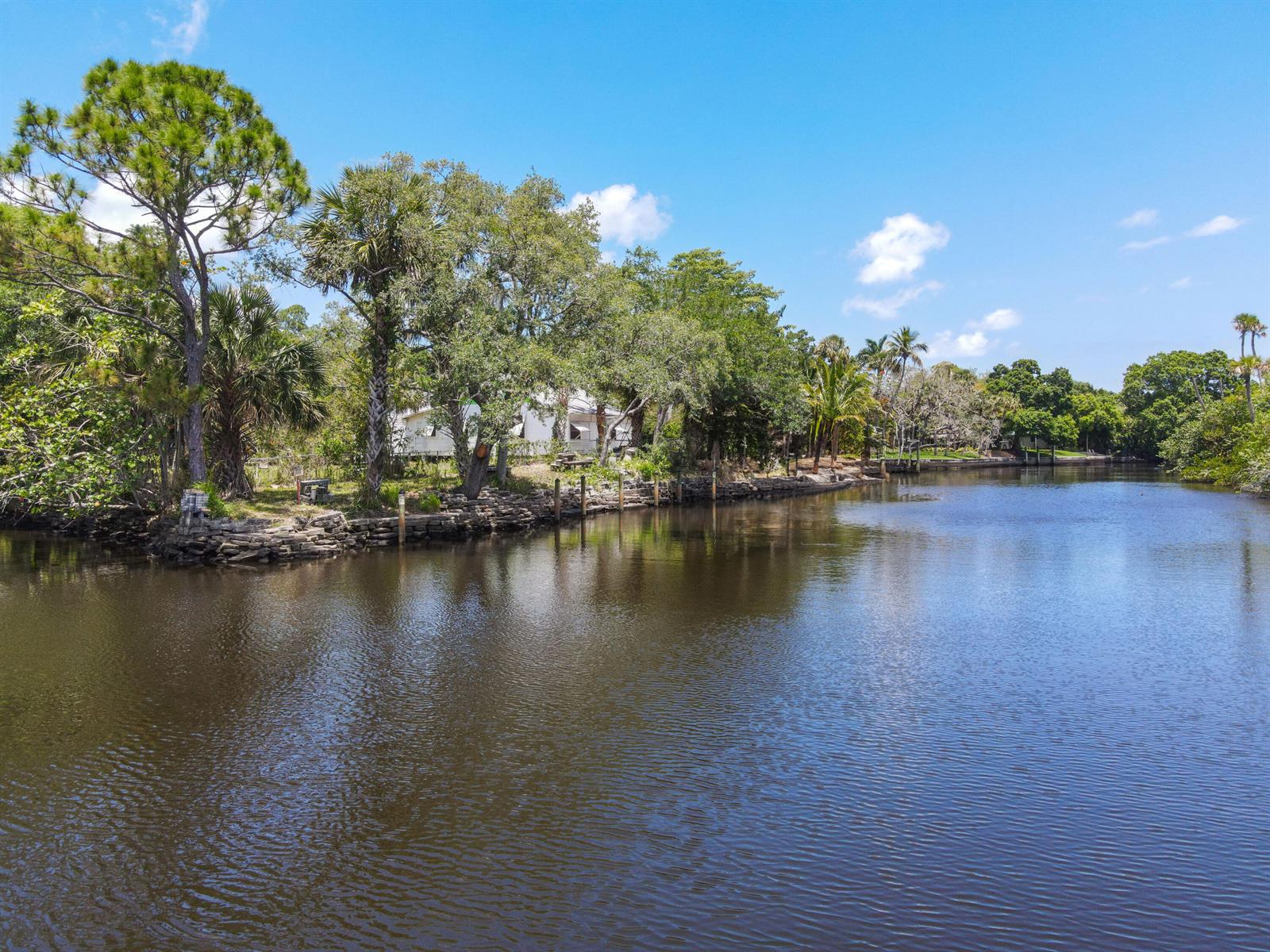 A calm canal flows past a stone-retained shoreline lined with mature trees and vegetation — 332 SW Salerno Road, Stuart FL 34997, STUART, FL