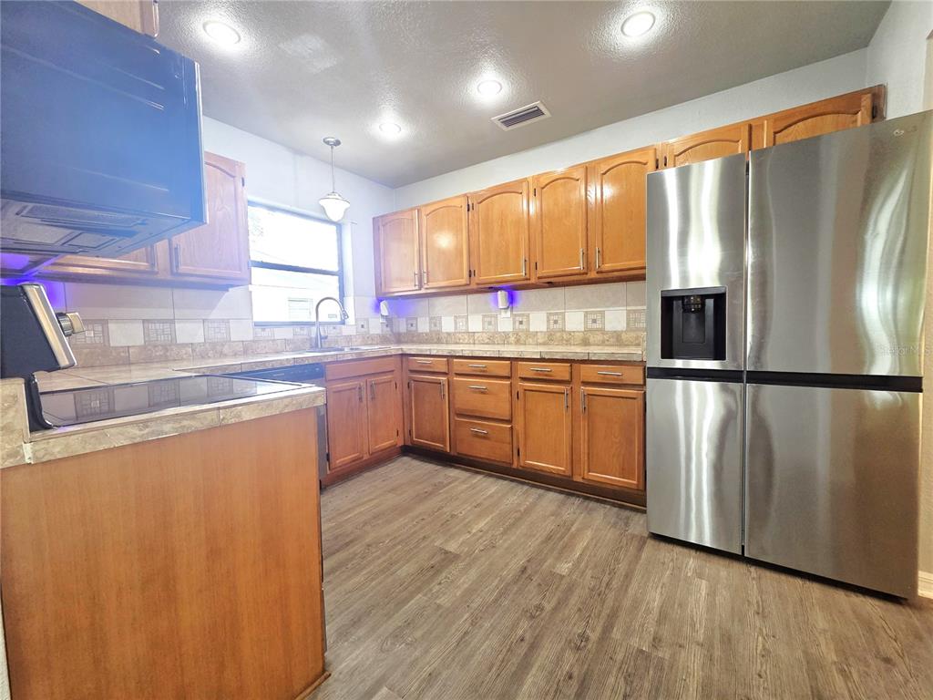 A kitchen features wood cabinets, stainless steel appliances, tile countertops, and wood-look flooring — 21390 LEHOUIER DRIVE, BROOKSVILLE, FL