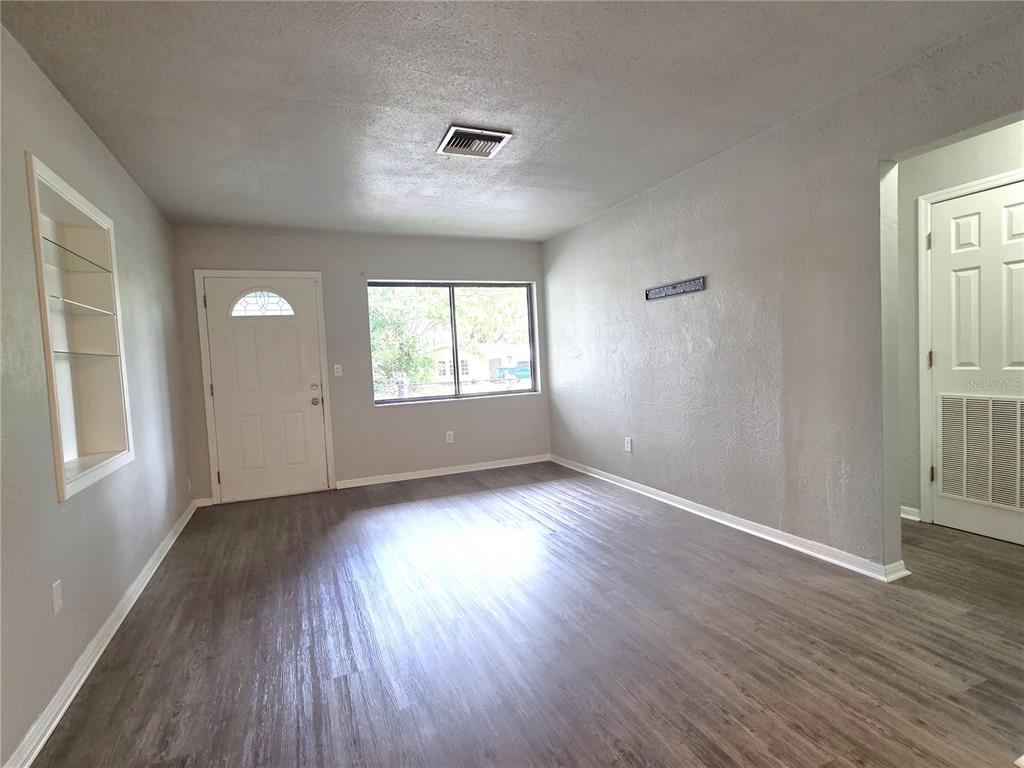 An empty living room features gray walls, wood-look flooring, a front door, and built-in shelving — 21390 LEHOUIER DRIVE, BROOKSVILLE, FL