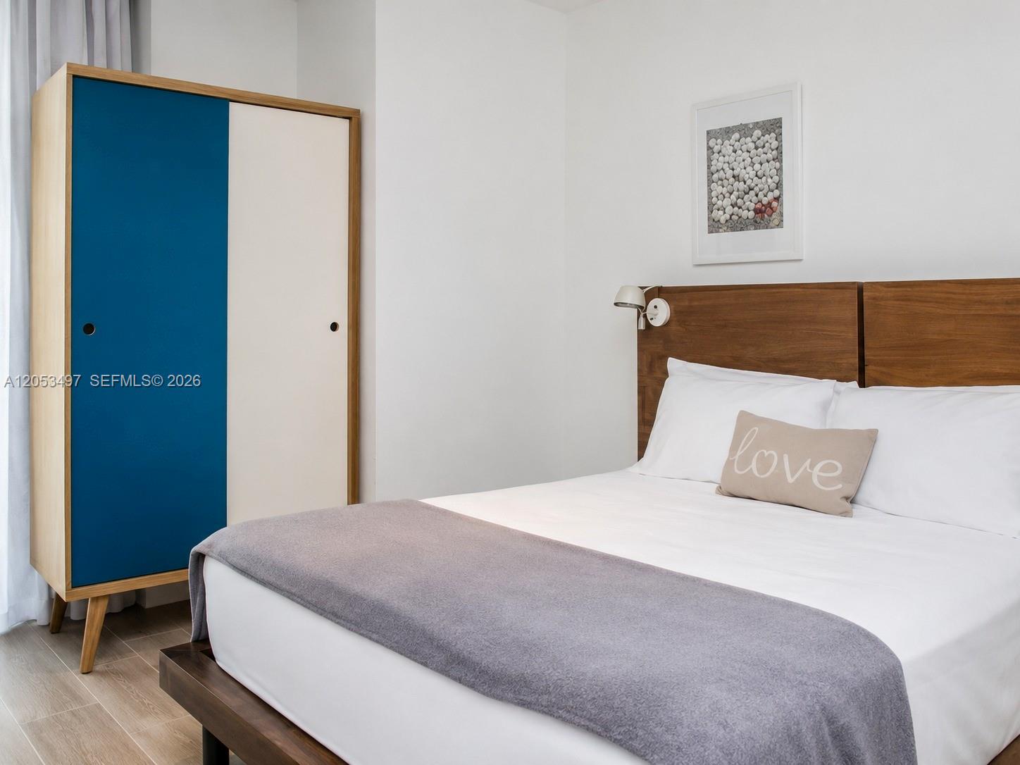 A bedroom features a bed with a wooden headboard, a grey throw, and a blue wardrobe — MIAMI BEACH, FL