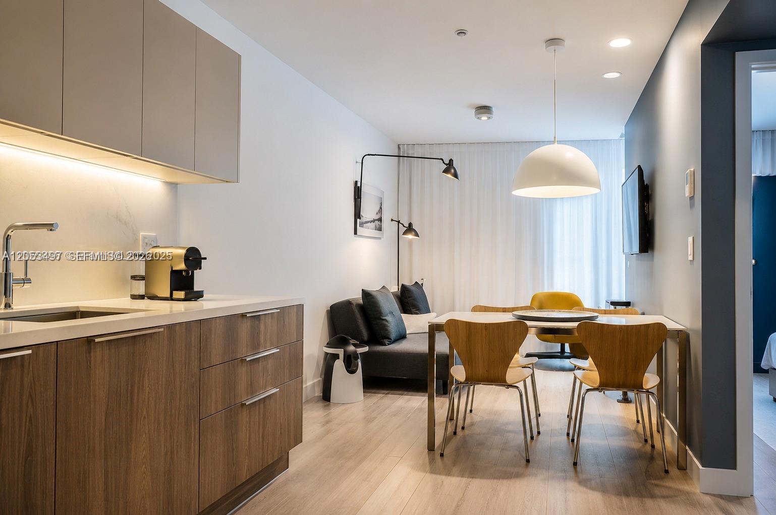A modern kitchen and dining area features wood cabinets, a sofa, and a dining table — MIAMI BEACH, FL