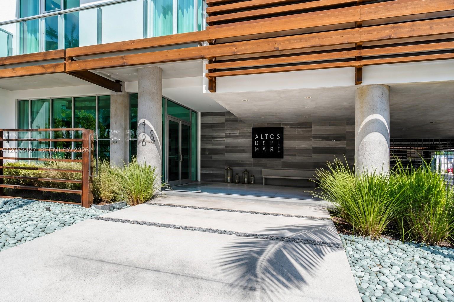 The entrance of a modern building features concrete columns, wood slats, and a stone wall — MIAMI BEACH, FL