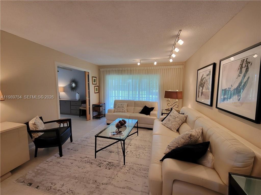 A living room features two white sofas, a glass coffee table, and track lighting — 3774 Inverrary Blvd # 103P, Lauderhill FL 33319, LAUDERHILL, FL