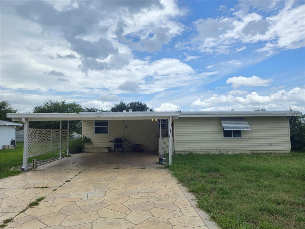 A single-story house with light siding, a stone-patterned driveway, and an attached carport — 6605 NE 1ST LANE, OCALA, FL