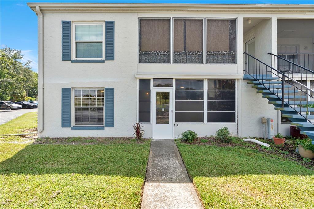 A two-story apartment building exterior features a ground-floor entrance, screened windows, and blue shutters — 1018 PLANTATION DRIVE UNIT A18, KISSIMMEE, FL