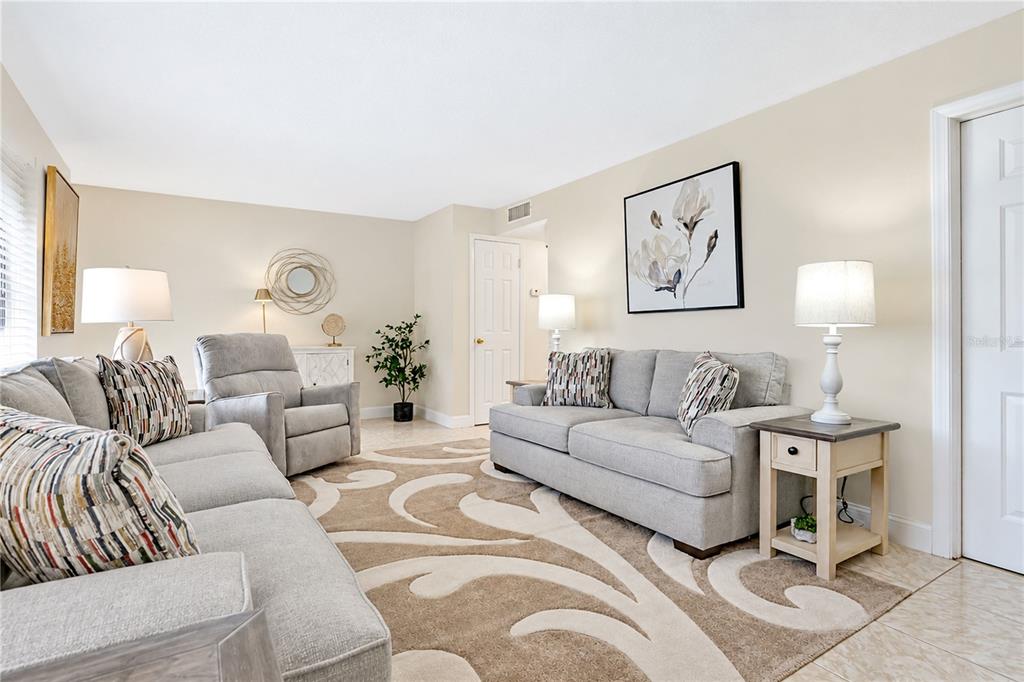 A living room features gray sofas, a patterned area rug, and light-colored tile flooring — 1018 PLANTATION DRIVE UNIT A18, KISSIMMEE, FL