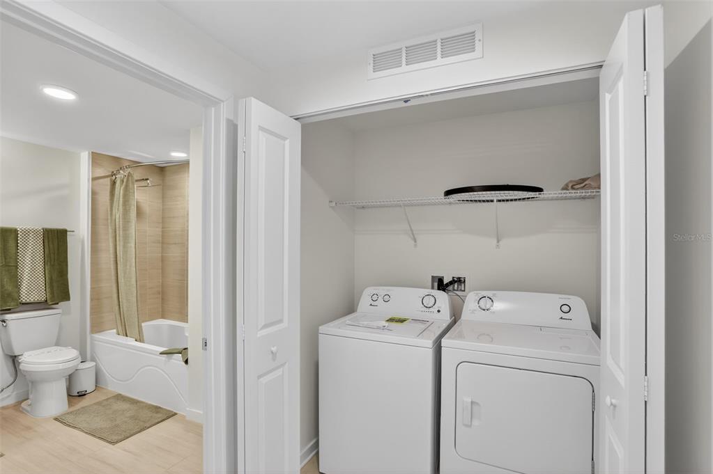 A laundry closet with a washer and dryer sits adjacent to a full bathroom — 5579 MILLENIA PARK BOULEVARD UNIT 504, ORLANDO, FL