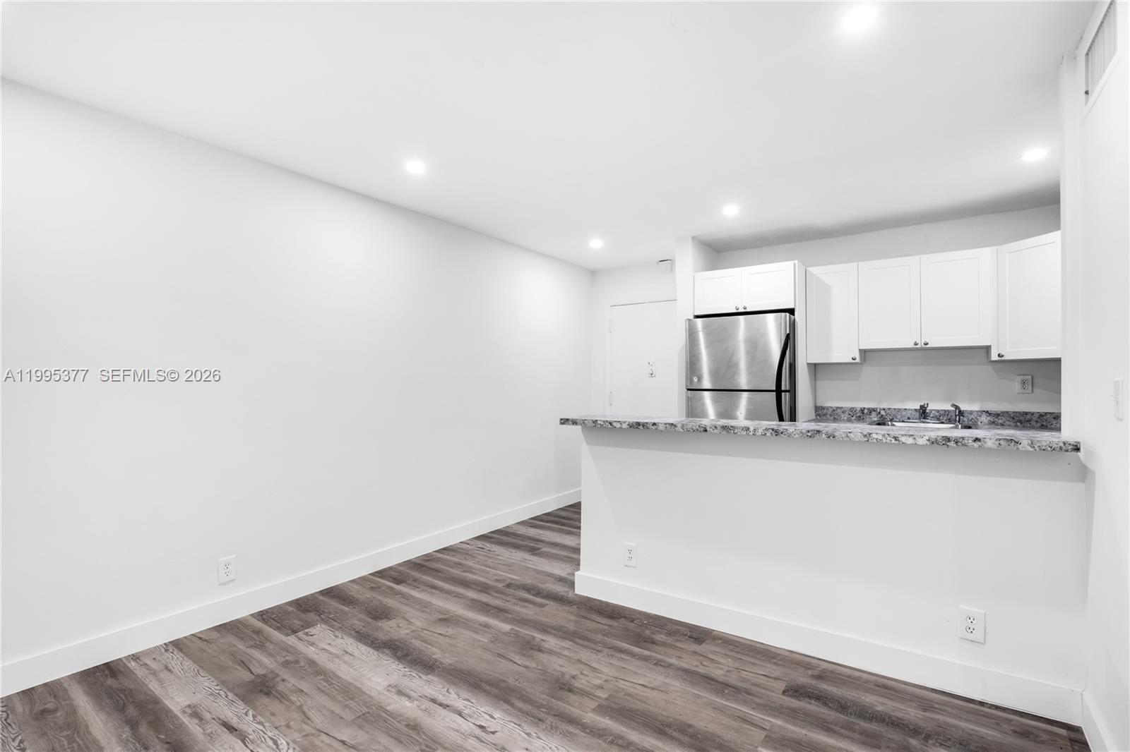 A kitchen with white cabinets and a granite countertop overlooks a wood-floored living area — 6445 NW 2nd Ave # 2, Miami FL 33150, MIAMI, FL