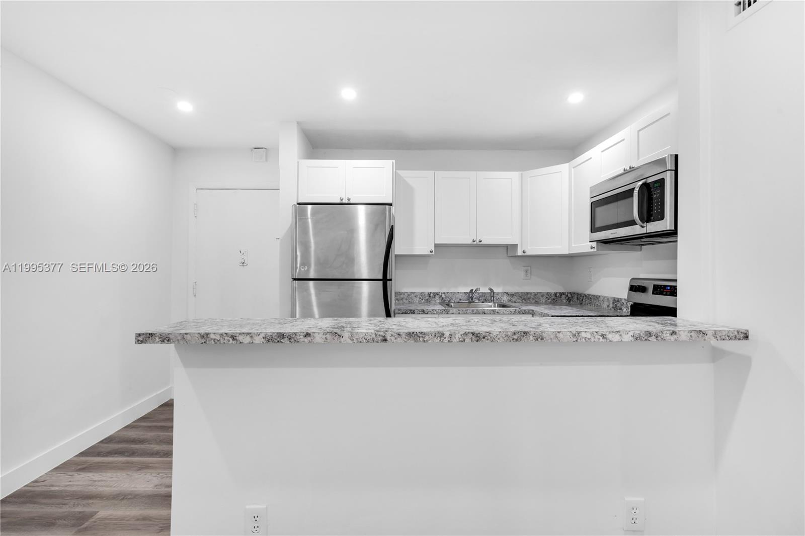 A kitchen features white cabinets, stainless steel appliances, and a granite-look breakfast bar — 6445 NW 2nd Ave # 2, Miami FL 33150, MIAMI, FL