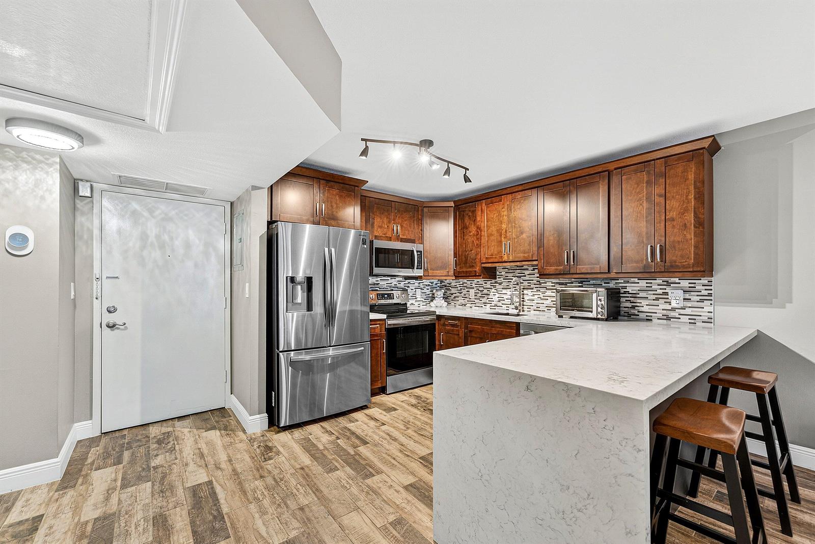 A kitchen features dark wood cabinets, stainless steel appliances, and a white quartz breakfast bar — 101 E Mcnab Road # 304, Pompano Beach FL 33060, POMPANO BEACH, FL