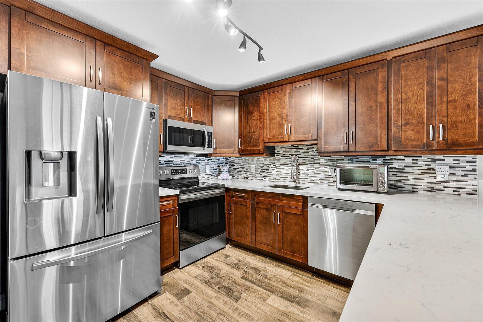 A kitchen features dark wood cabinets, stainless steel appliances, and a light-colored stone countertop — 101 E Mcnab Road # 304, Pompano Beach FL 33060, POMPANO BEACH, FL