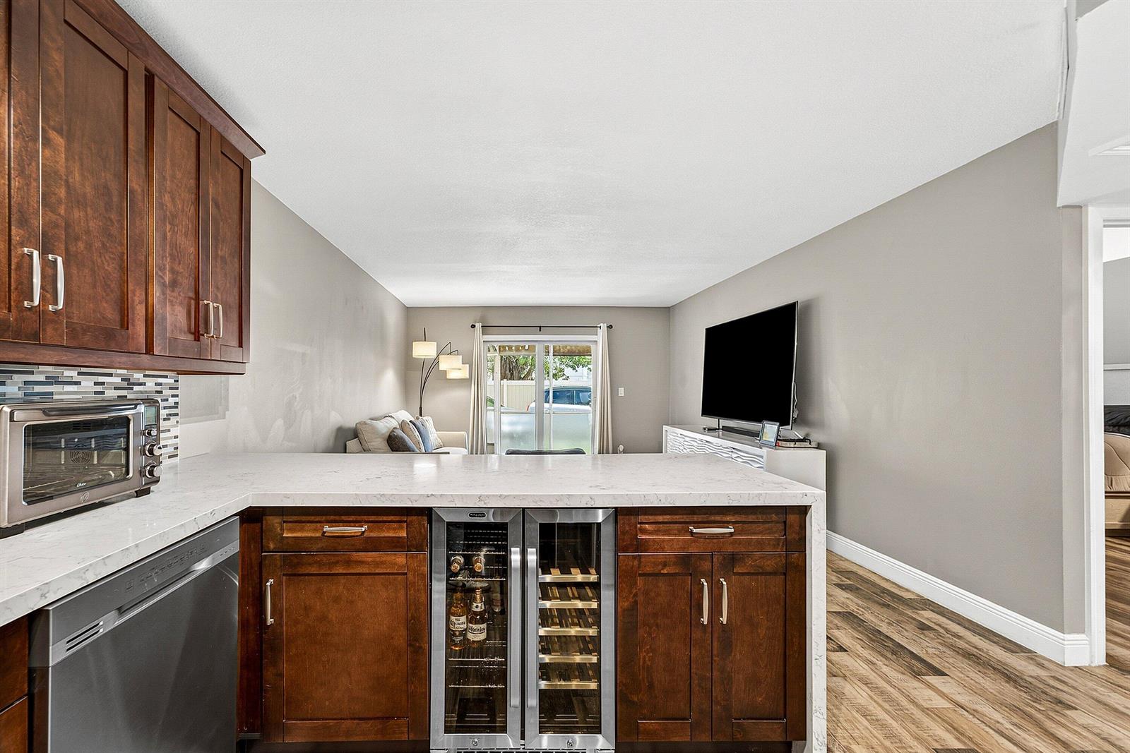 A kitchen island with a wine cooler faces a living area with a television — 101 E Mcnab Road # 304, Pompano Beach FL 33060, POMPANO BEACH, FL