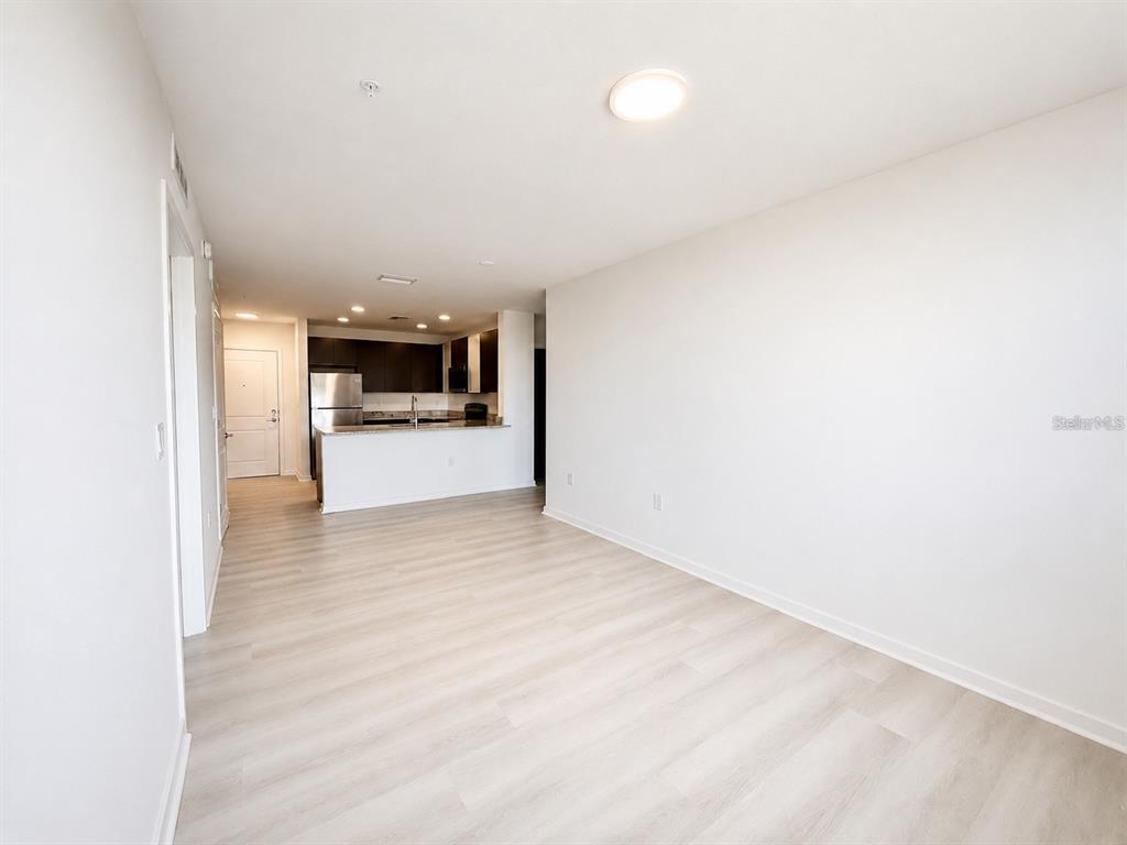 An open-concept living area features light wood-look flooring and a view into the kitchen — 5587 MILLENIA PARK BOULEVARD UNIT 316, ORLANDO, FL