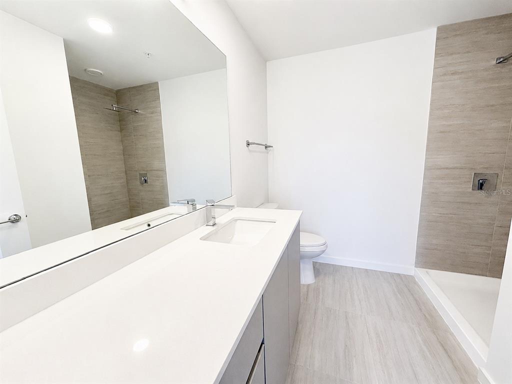 A modern bathroom features a white vanity, a large mirror, a toilet, and a tiled shower — 5587 MILLENIA PARK BOULEVARD UNIT 316, ORLANDO, FL