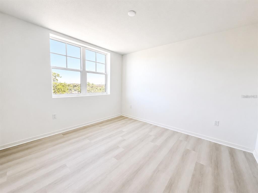 An empty bedroom features white walls, light wood-look flooring, and a large window — 5587 MILLENIA PARK BOULEVARD UNIT 316, ORLANDO, FL