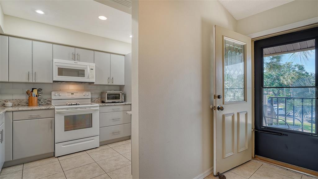 A kitchen with light gray cabinets and white appliances opens to an exterior door — 4462 WEYBRIDGE STREET UNIT 72, SARASOTA, FL