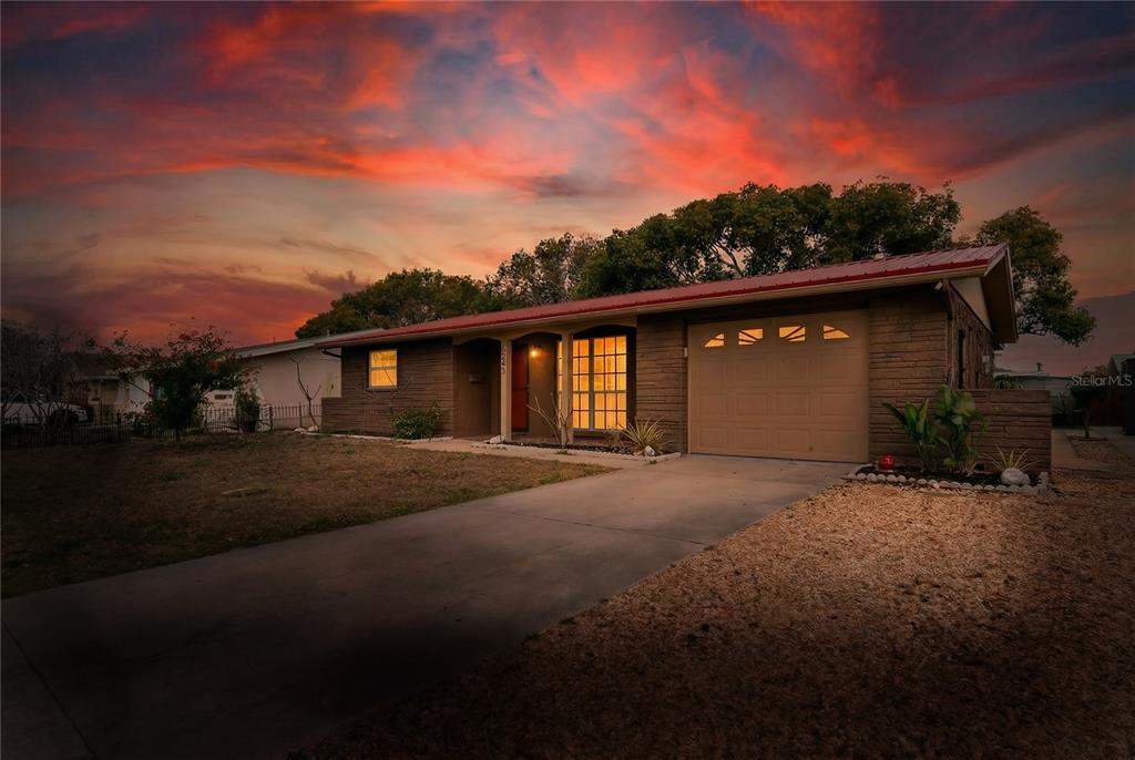 A single-story brick house with a red metal roof and a concrete driveway at sunset — 6805 ALTAVISTA STREET, PORT RICHEY, FL