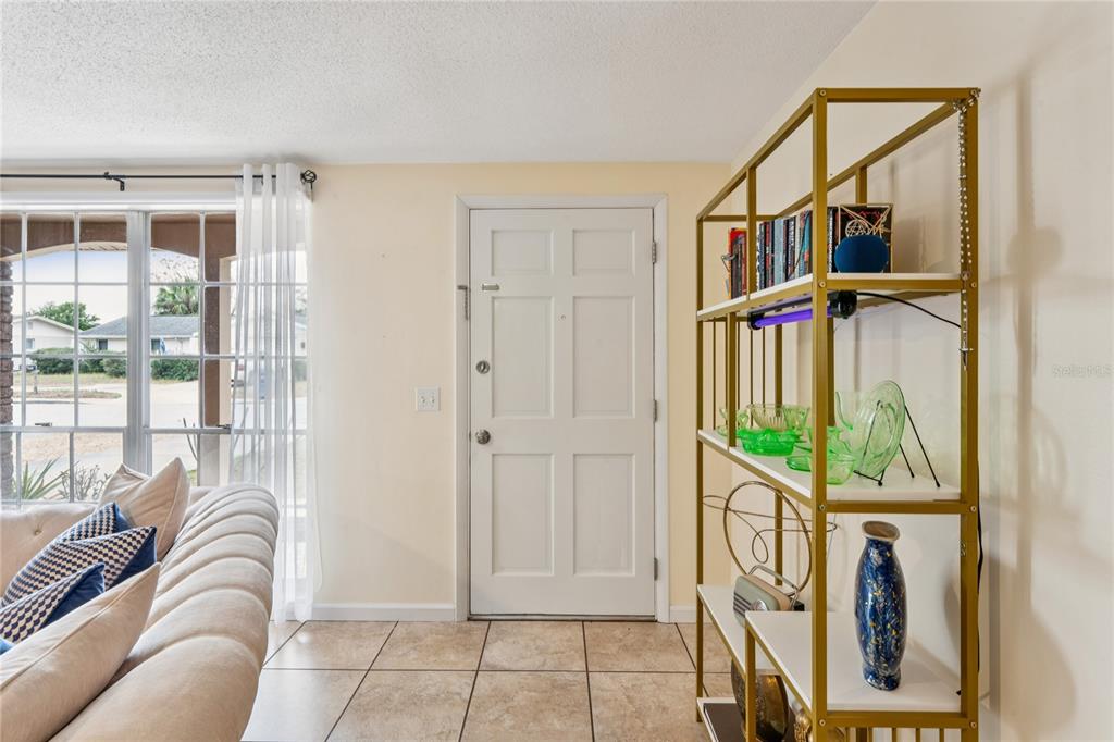 A living room features a white front door, tiled floors, and a gold metal shelving unit — 6805 ALTAVISTA STREET, PORT RICHEY, FL