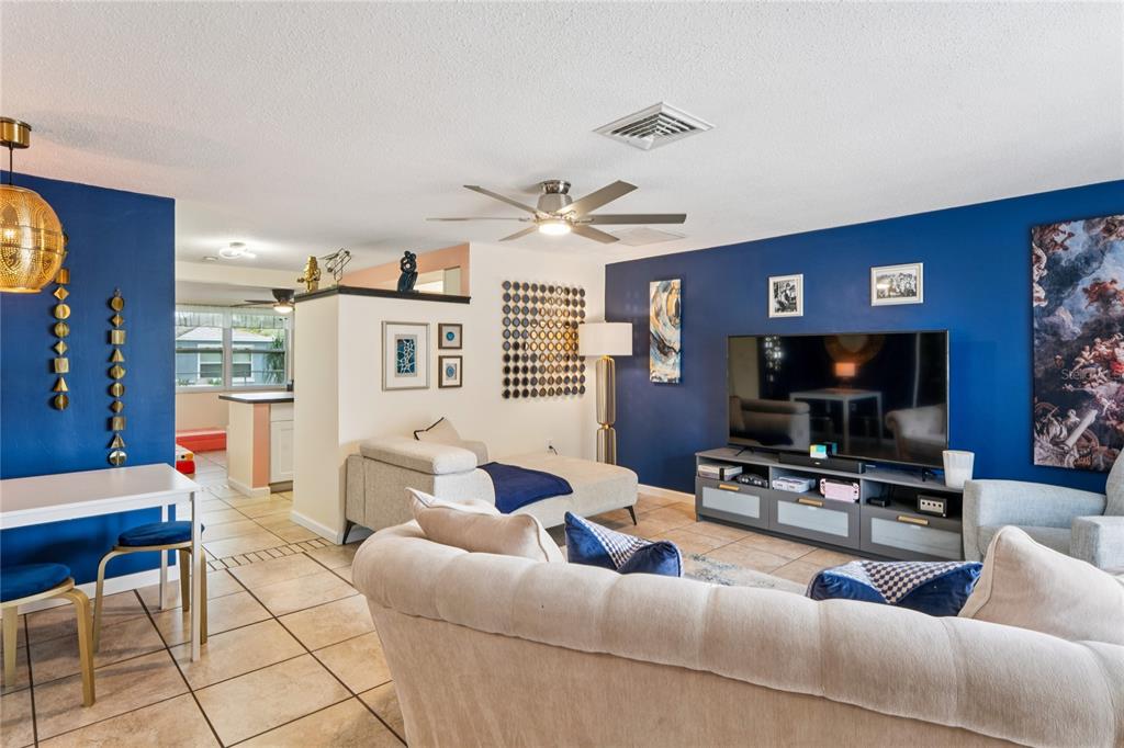 A living room with blue walls, tile flooring, a ceiling fan, and a large television — 6805 ALTAVISTA STREET, PORT RICHEY, FL