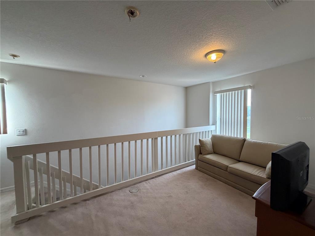 A carpeted loft area features a beige sofa, a white railing, and a ceiling light — 456 WATERFORD WAY, KISSIMMEE, FL
