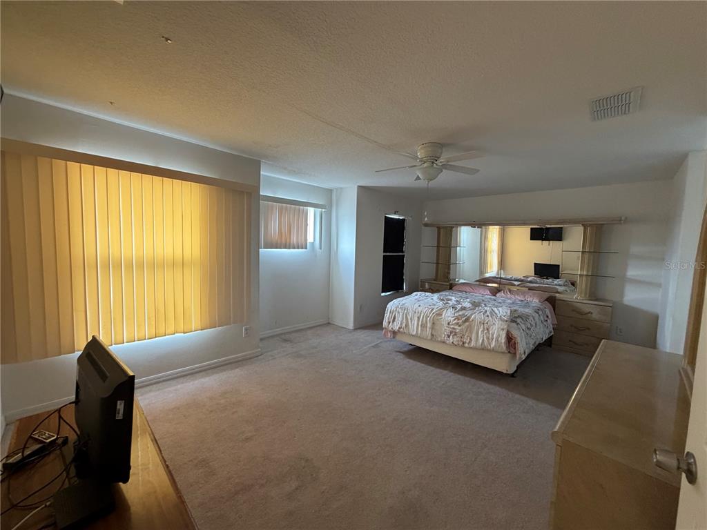A bedroom features beige carpeting, a bed with a mirrored headboard, and vertical window blinds — 456 WATERFORD WAY, KISSIMMEE, FL