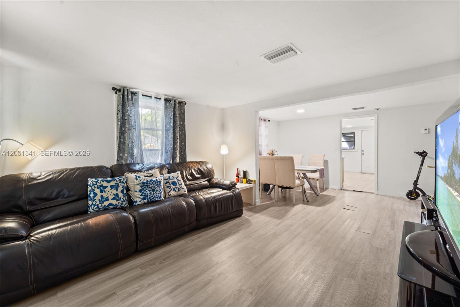 A living room with a dark leather sofa, light wood flooring, and an adjacent dining area — 349 NW 41st St, Miami FL 33127, MIAMI, FL