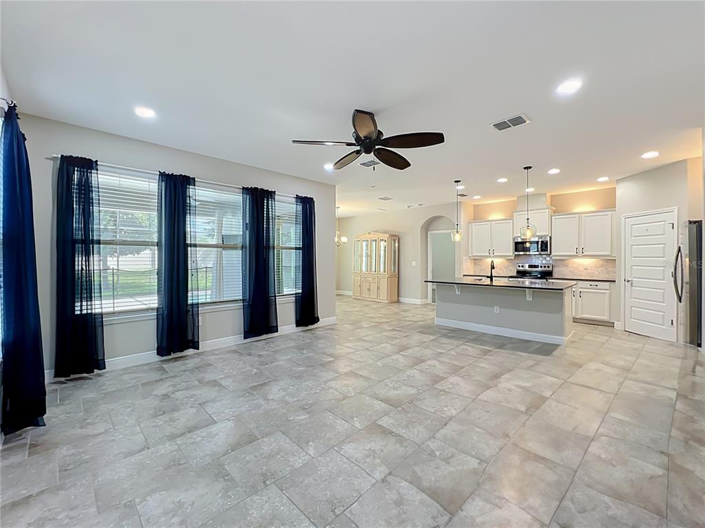 An open-concept living area features tile flooring, a kitchen island, and large windows with curtains — 16131 HAMPTON CROSSING DRIVE, WINTER GARDEN, FL