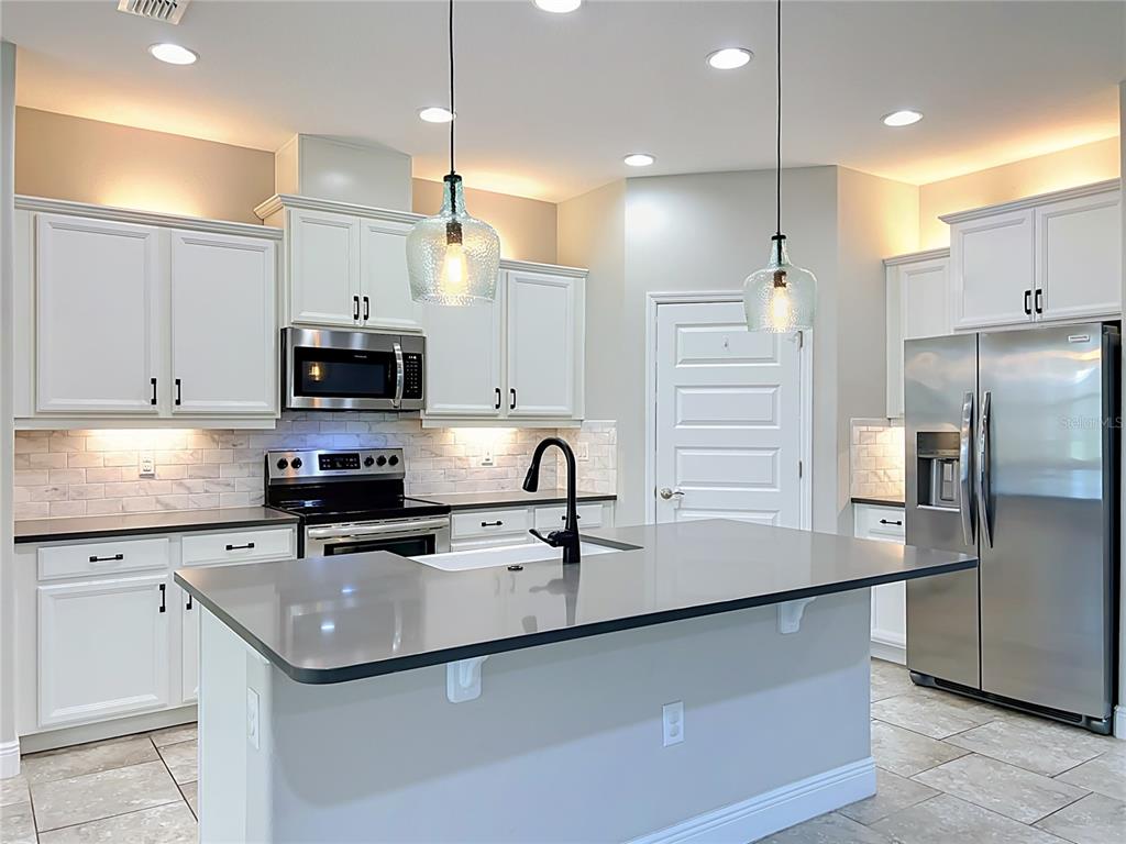 A kitchen features white cabinets, stainless steel appliances, a gray island, and two glass pendants — 16131 HAMPTON CROSSING DRIVE, WINTER GARDEN, FL