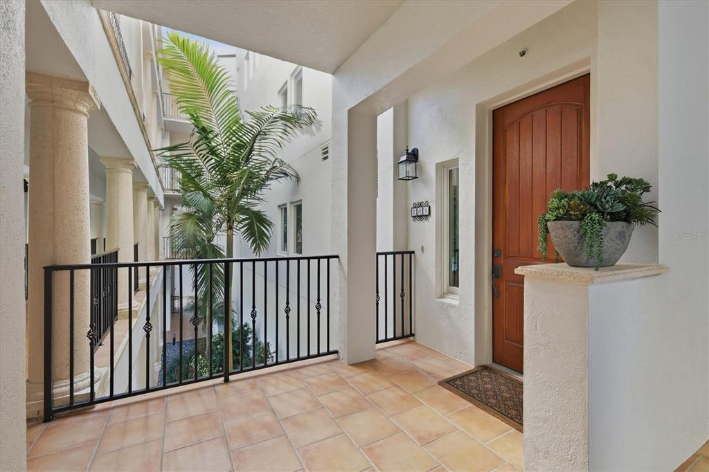 A tiled balcony features a wooden door, a potted plant, and a black metal railing — 11200 HACIENDA DEL MAR BOULEVARD UNIT B-204, PLACIDA, FL