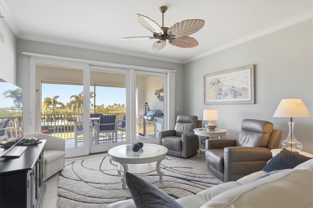 A living room features a palm-leaf ceiling fan, gray leather armchairs, and a sliding glass door — 11200 HACIENDA DEL MAR BOULEVARD UNIT B-204, PLACIDA, FL