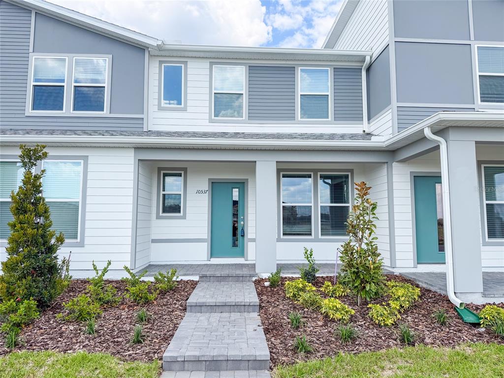A two-story townhouse exterior features gray and white siding, a teal front door, and landscaping — 10537 GLOWING BEACON STREET, ORLANDO, FL