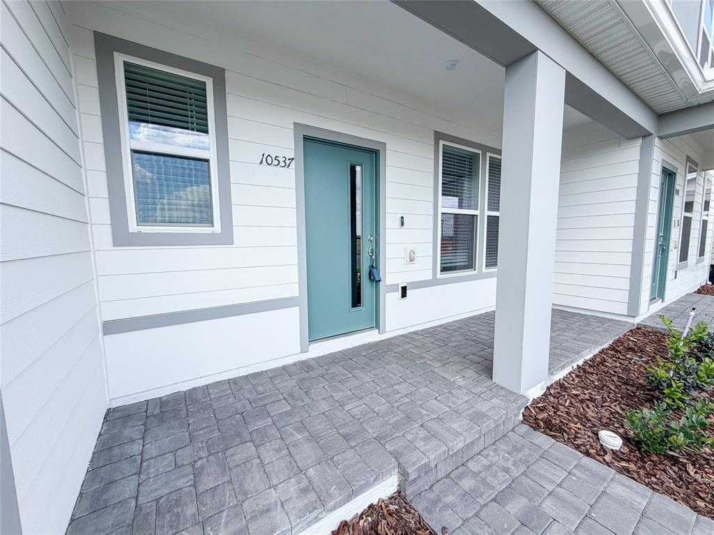 A teal front door with a vertical window sits on a paved porch of a house — 10537 GLOWING BEACON STREET, ORLANDO, FL