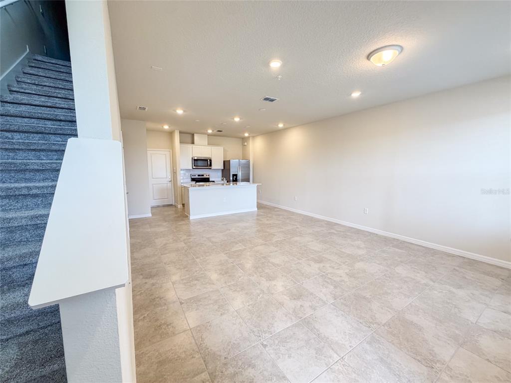 An open-concept kitchen with white cabinets and a breakfast bar overlooks a tiled living area — 10537 GLOWING BEACON STREET, ORLANDO, FL