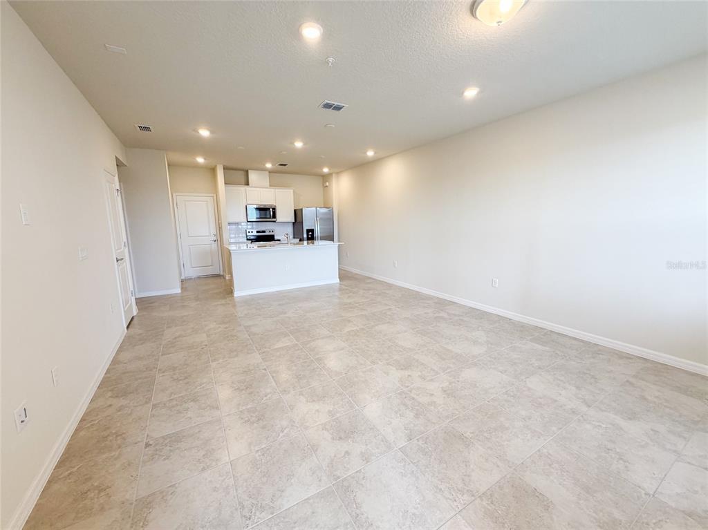 An open-concept living area features light-colored tile flooring and a kitchen with white cabinetry — 10537 GLOWING BEACON STREET, ORLANDO, FL