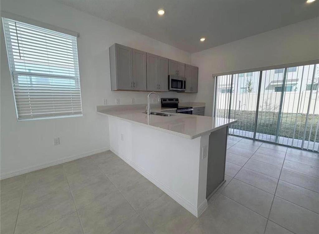A kitchen with gray cabinets, a white island, and a sliding glass door to outside — 3356 COMPOSITION STREET, KISSIMMEE, FL