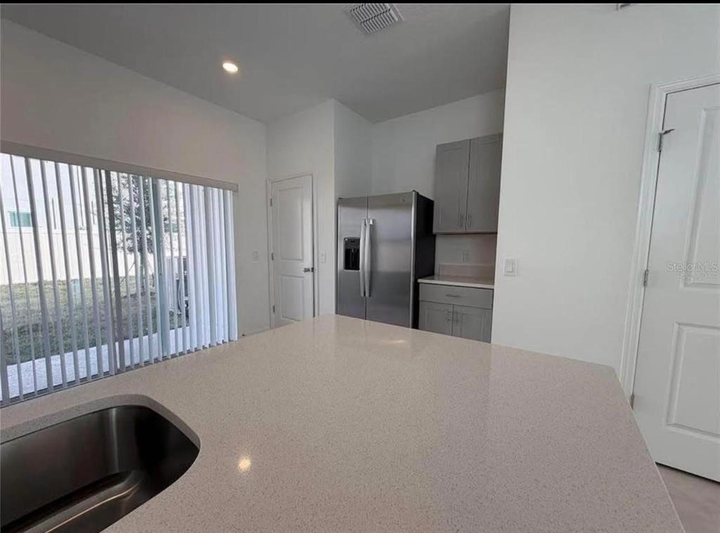 A kitchen island with a sink overlooks a refrigerator and gray cabinets — 3356 COMPOSITION STREET, KISSIMMEE, FL