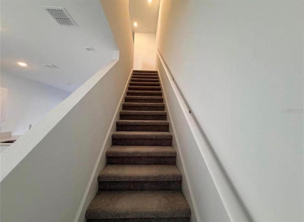 A carpeted staircase with white walls and a handrail leads to an upper landing — 3356 COMPOSITION STREET, KISSIMMEE, FL