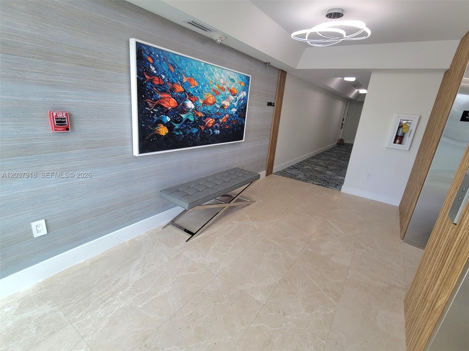 A modern hallway features a gray textured wall, a fish painting, a bench, and tile flooring — 5880 Collins Ave # 302, Miami Beach FL 33140, MIAMI BEACH, FL