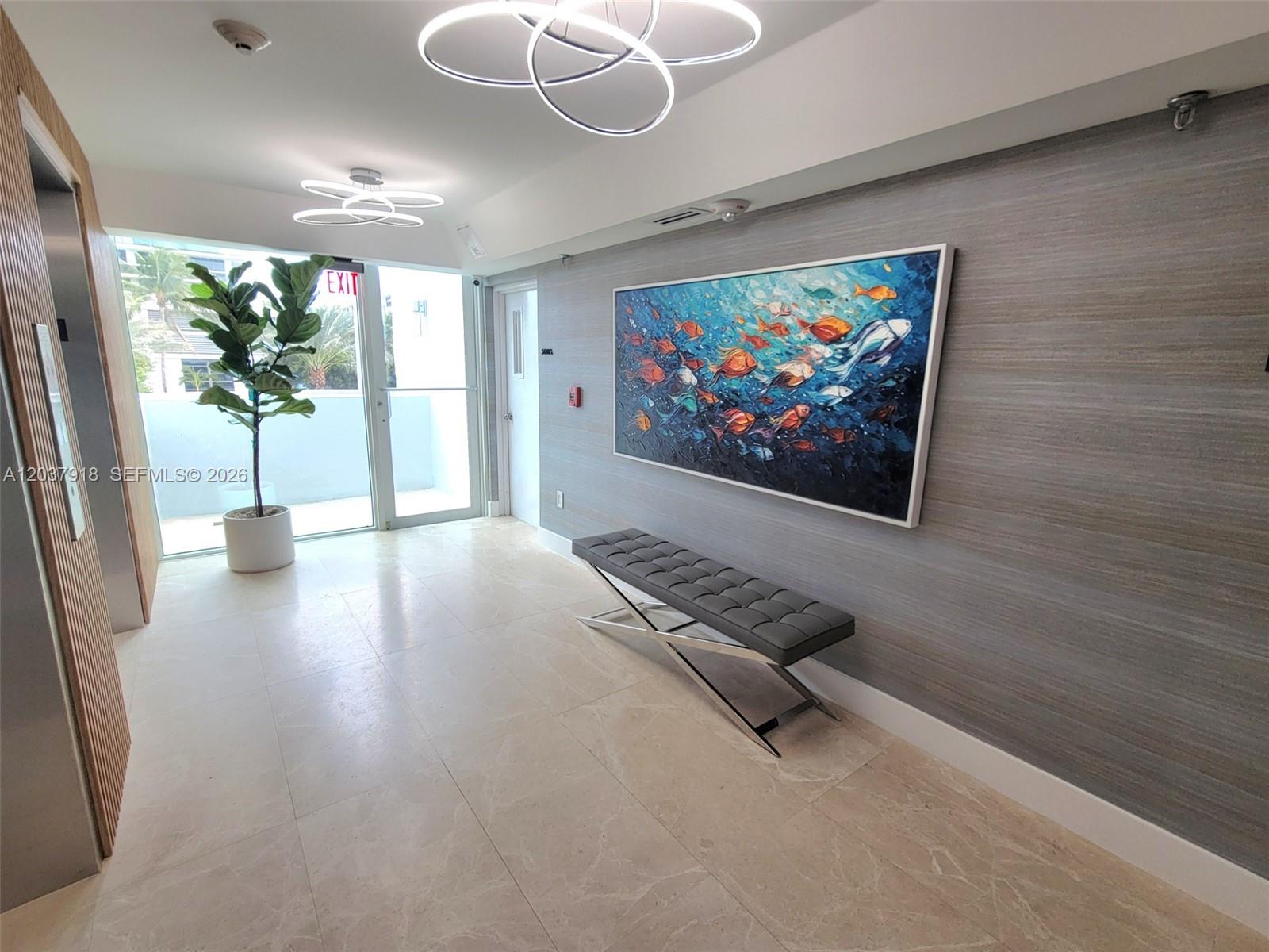 A modern lobby features a gray textured wall, a bench, fish artwork, and circular lighting — 5880 Collins Ave # 302, Miami Beach FL 33140, MIAMI BEACH, FL