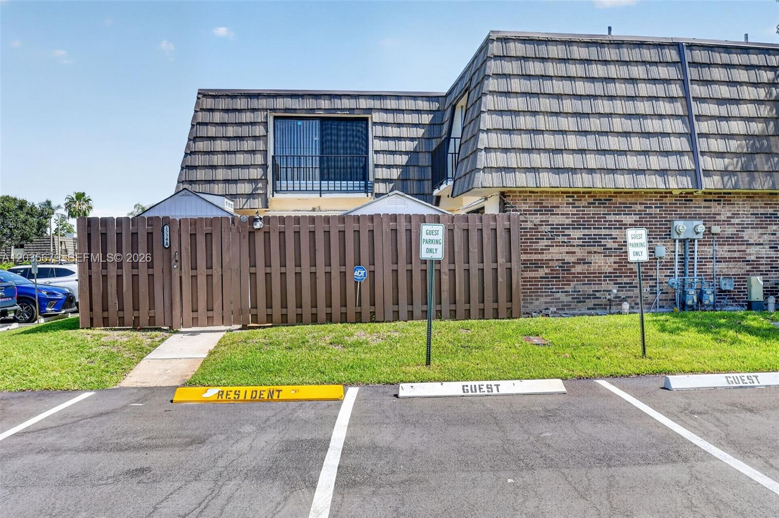 A two-story building exterior features a brown wooden fence, guest parking spaces, and a balcony — 1534 Forest Lakes Cir # A, West Palm Beach FL 33406, WEST PALM BEACH, FL