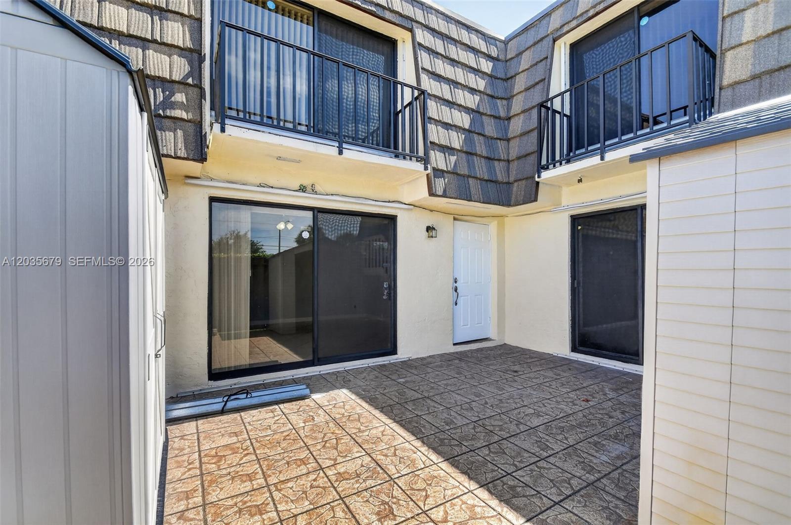 A paved patio area sits between two building sections with sliding glass doors and balconies — 1534 Forest Lakes Cir # A, West Palm Beach FL 33406, WEST PALM BEACH, FL